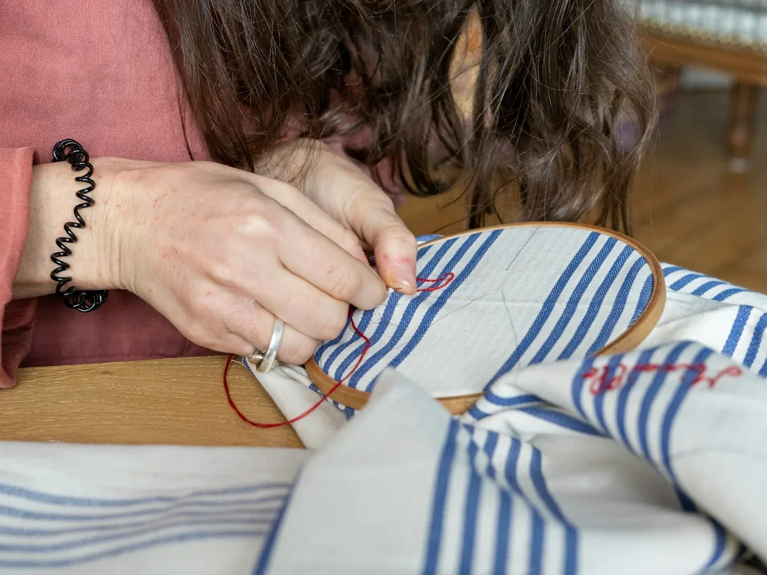 Mani al lavoro su un tessuto teso, con ago e filo durante un ricamo a mano
